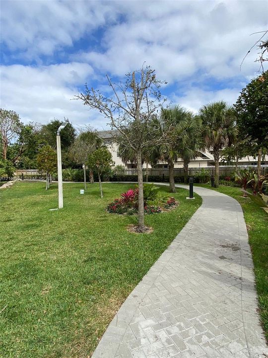 Landscaped grounds featuring a paved herringbone-pattern walkway, mature palm trees, manicured turf, and dedicated path lighting