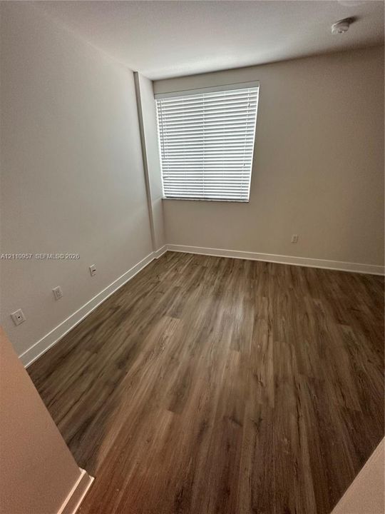 Neutral-toned walls paired with wood-finish flooring and a single-pane window featuring installed horizontal blinds