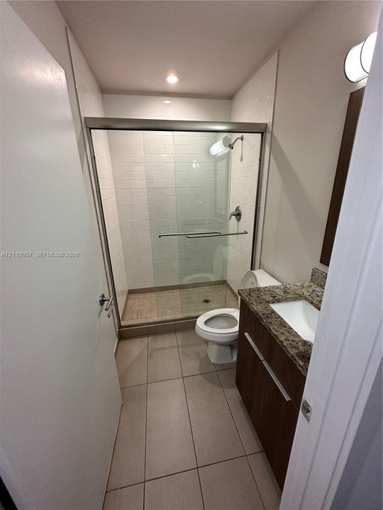 Bathroom featuring a glass-enclosed shower with subway tile surround, vanity with stone-finish countertop, undermount sink, and large-format tile flooring
