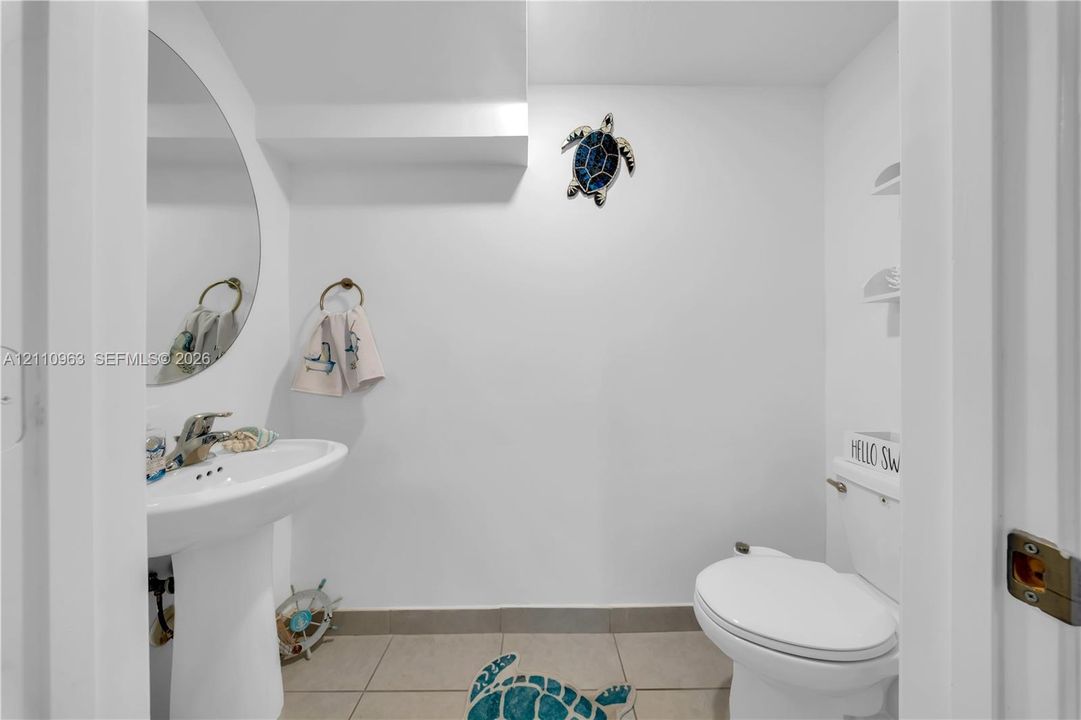 Powder room featuring a pedestal sink, arched wall mirror, ceramic tile flooring, and integrated shelving