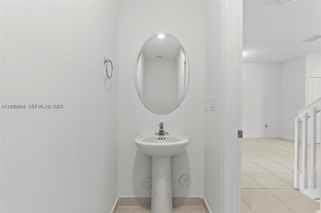 White porcelain pedestal sink with a chrome single-handle faucet, oval wall-mounted mirror, and wall-mounted metal towel ring