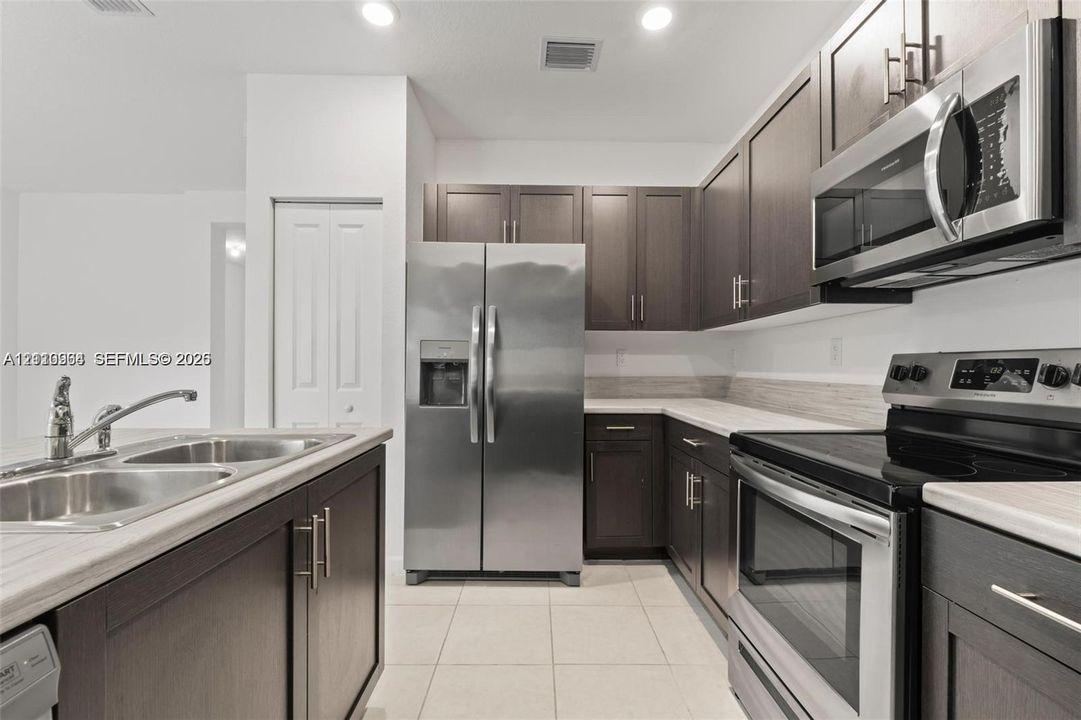Kitchen featuring dark-toned cabinetry, stainless steel appliances, light-toned countertops, tile flooring, and a dual-basin sink with a gooseneck faucet