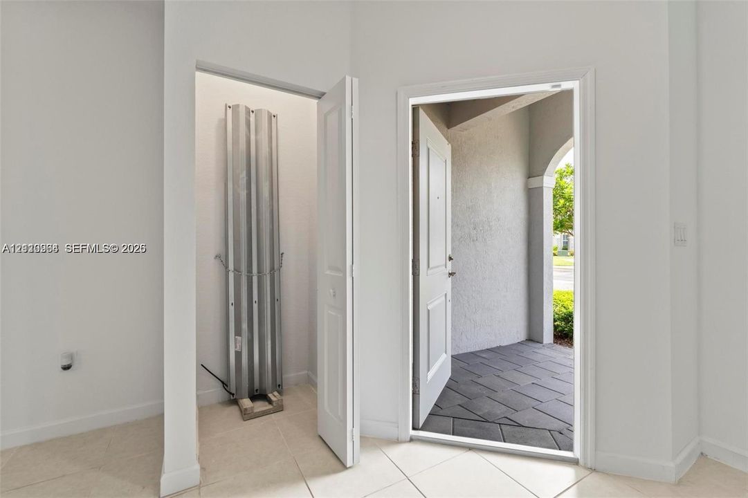 Entryway featuring large-format tile flooring, a storage closet, a white paneled door, and a tiled exterior porch with an arched architectural detail