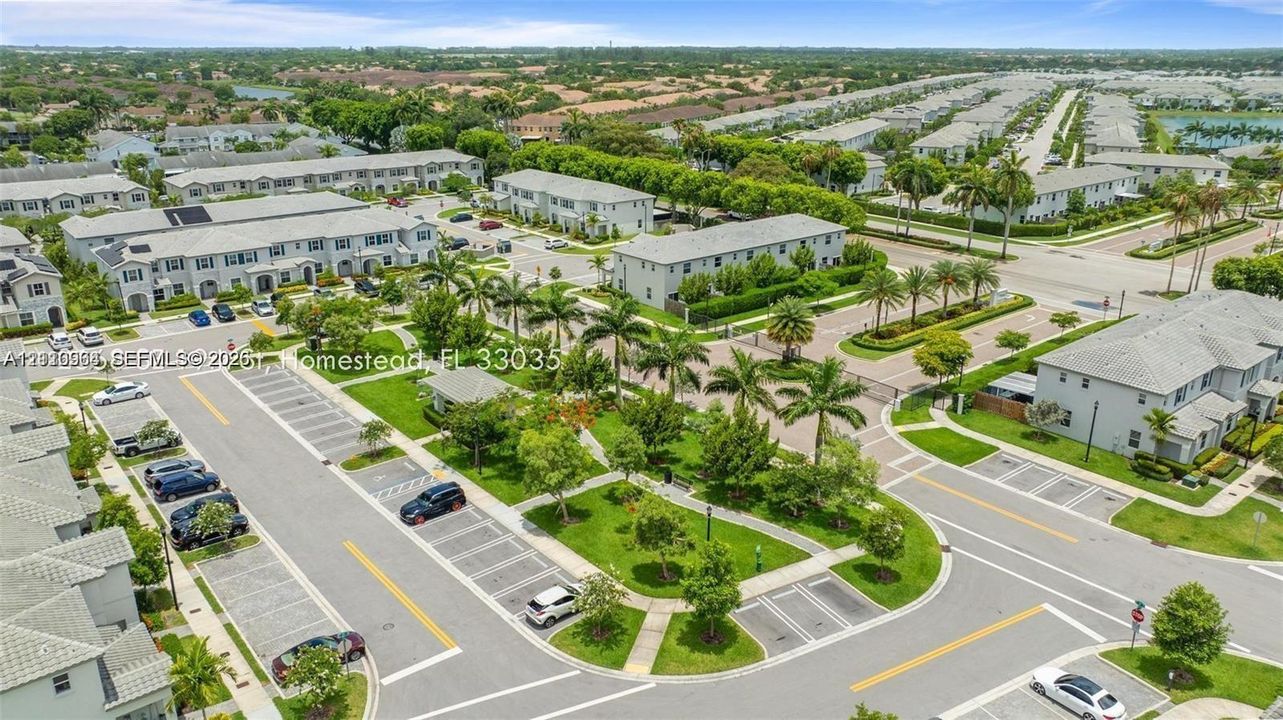 Aerial perspective of a multi-unit residential community featuring paved parking, manicured green space, mature palm trees, and sidewalk infrastructure