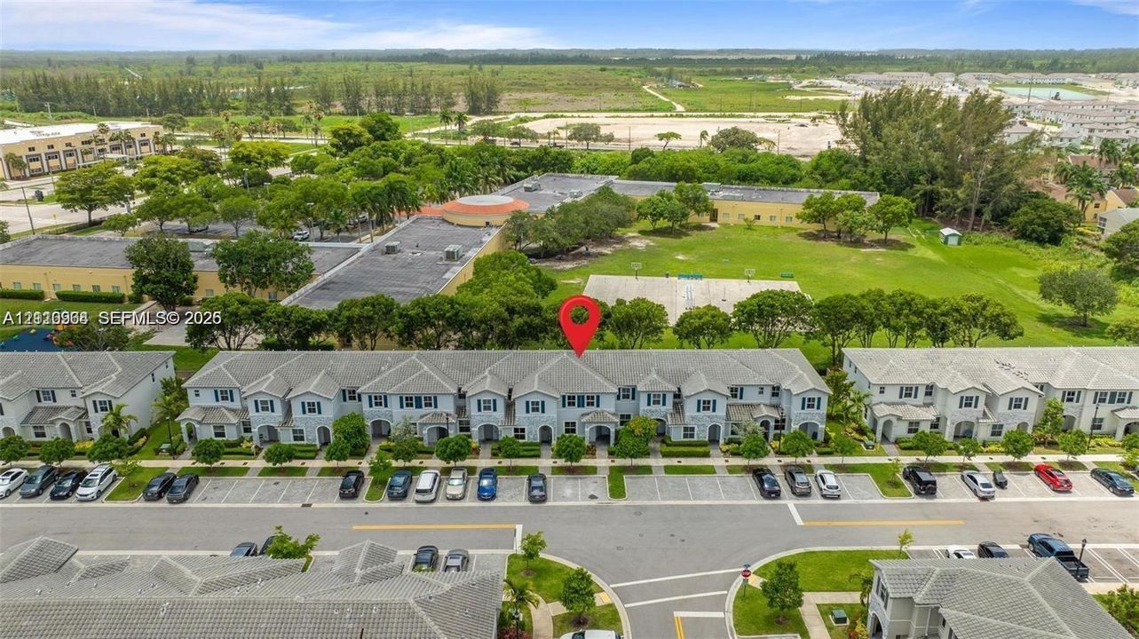 Aerial perspective of a multi-unit residential complex featuring gray shingle roofing, paved surface parking, and manicured landscaping