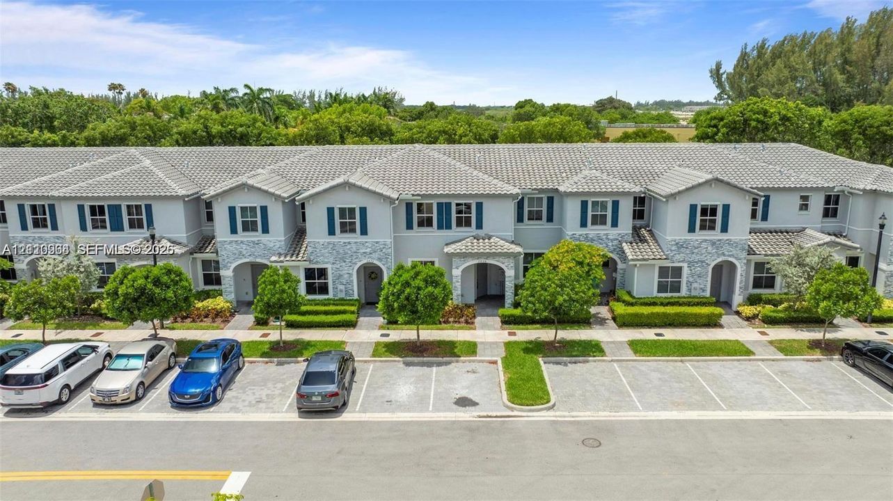 Two-story townhouse exterior featuring a concrete tile roof, stone facade accents, shuttered windows, and dedicated surface parking