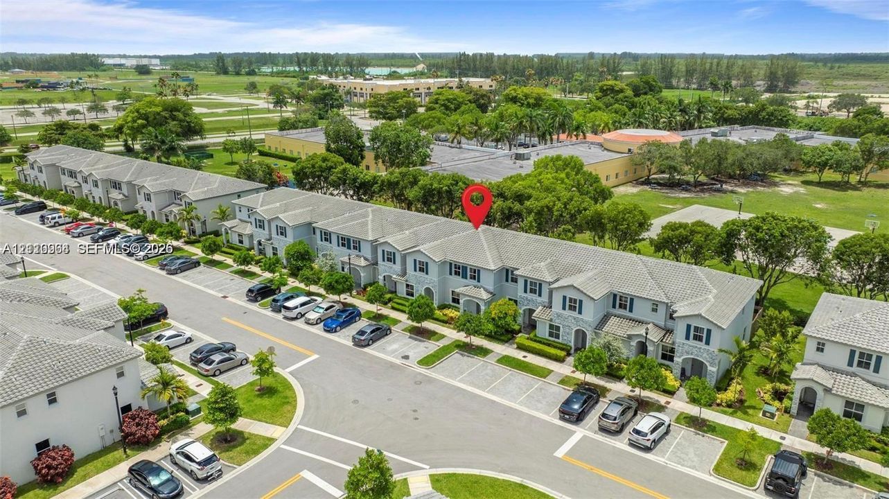 Aerial perspective of multi-story townhome featuring light-toned exterior finish, multi-pitched roofline, integrated parking spaces, and manicured landscape surrounding the building perimeter