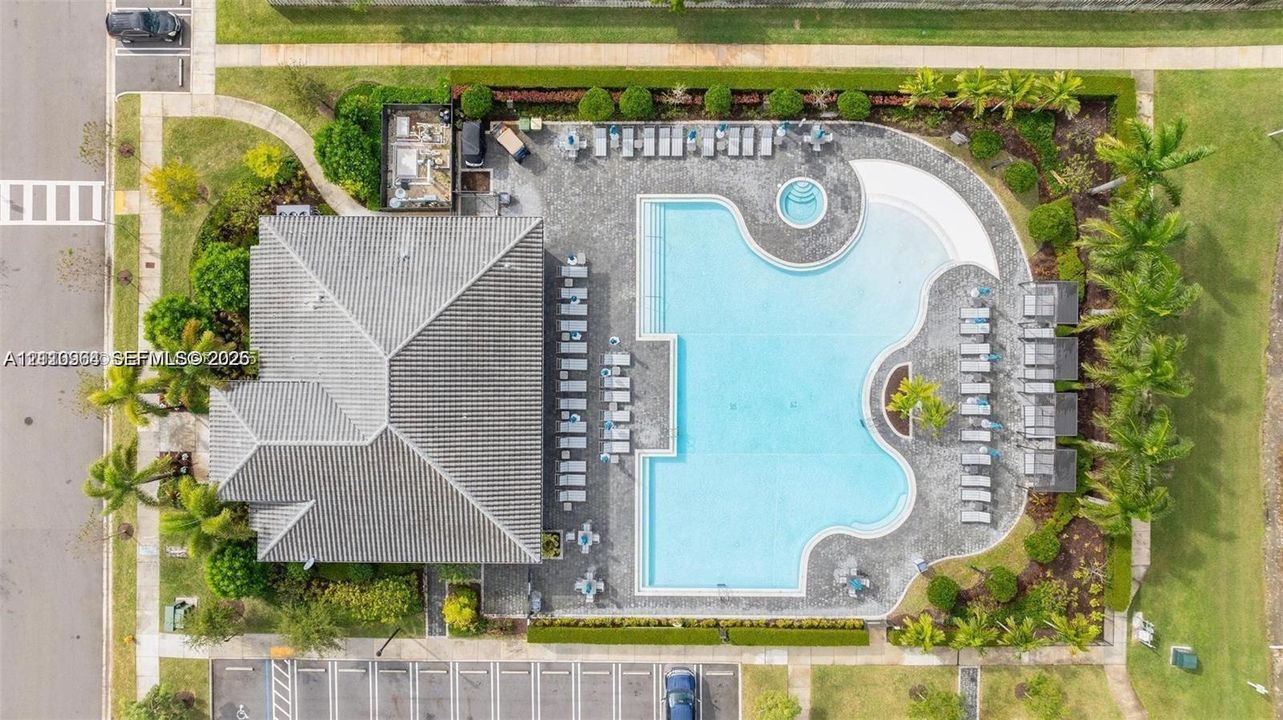 Aerial perspective of a community facility featuring a large swimming pool, an integrated spa, a paved deck, and mature landscaping