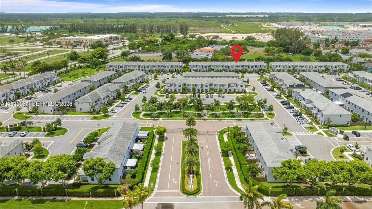 Aerial perspective of a multi-unit residential community featuring paved roadways, structured parking, landscaped medians, and mature palm trees