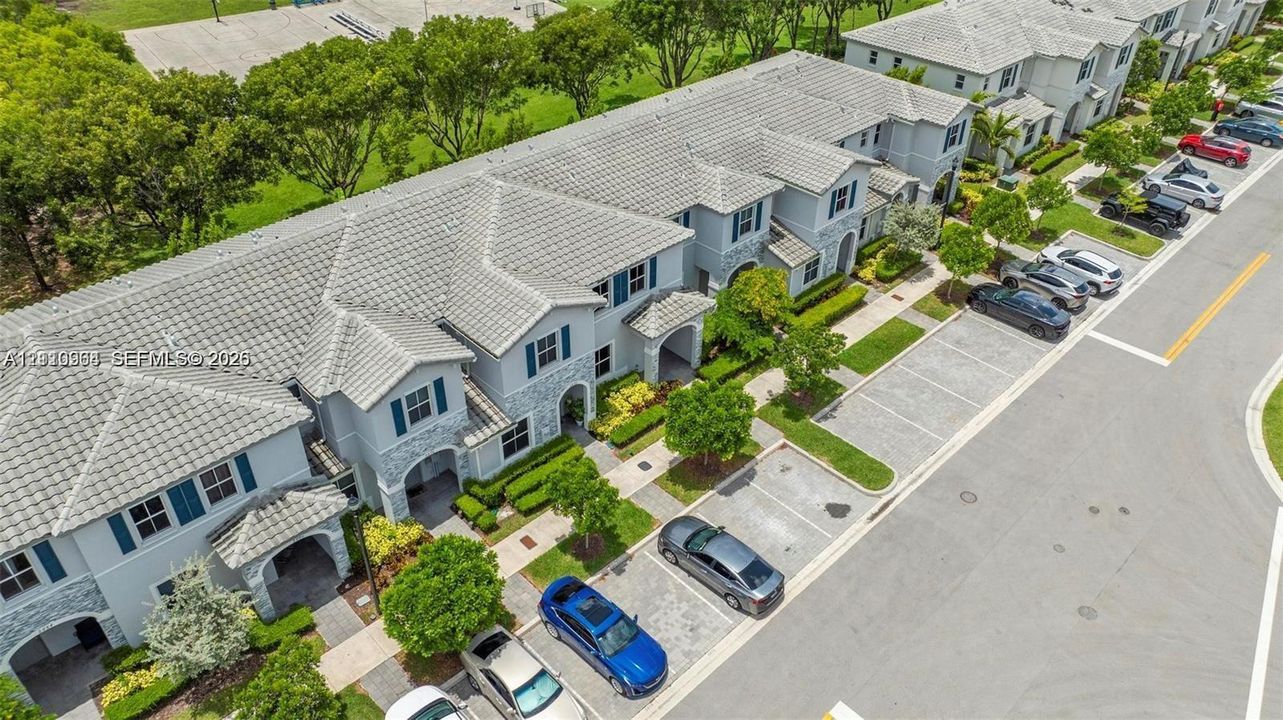 Multi-unit residential structure featuring a tiled roof, stone veneer exterior accents, shutter-trimmed windows, and paver-style private parking areas