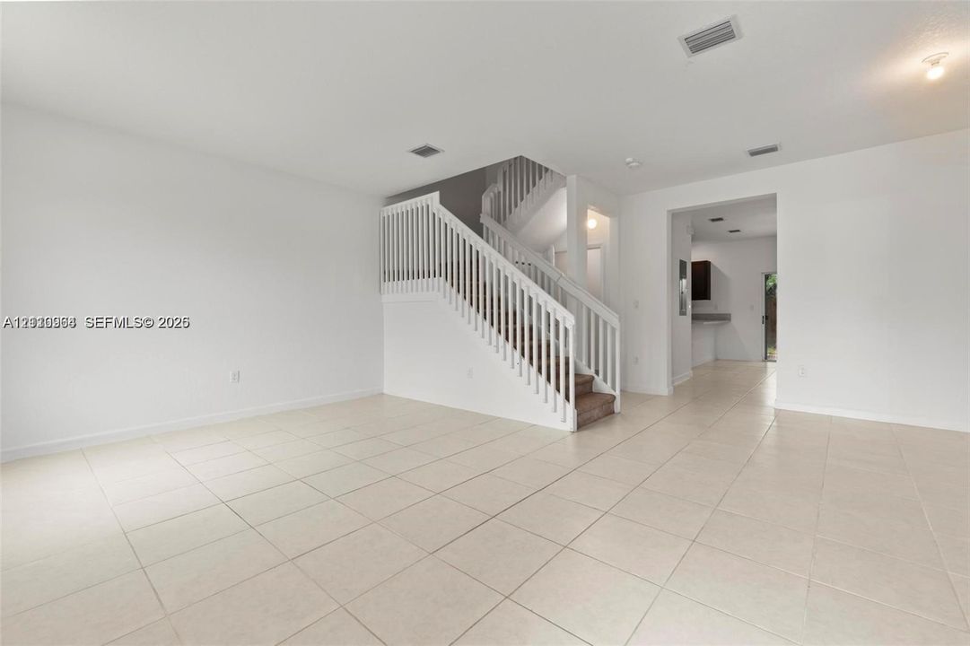 Open interior space featuring neutral tile flooring, staircase with white railing, and flush-mount ceiling lighting