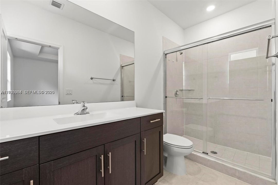 Bathroom featuring a dark wood-finish vanity with a white countertop, large wall-spanning mirror, and a glass-enclosed shower with tiled walls