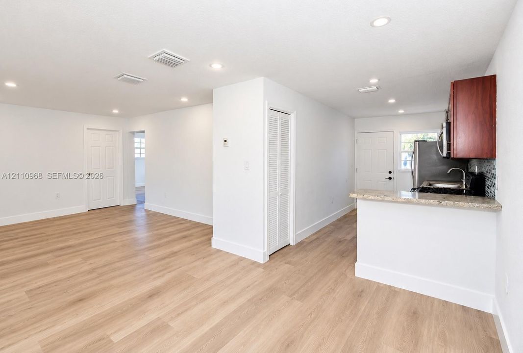 Open-concept interior featuring light wood-finish flooring, recessed lighting, breakfast bar with stone-finish countertop, and built-in louvered-door closet