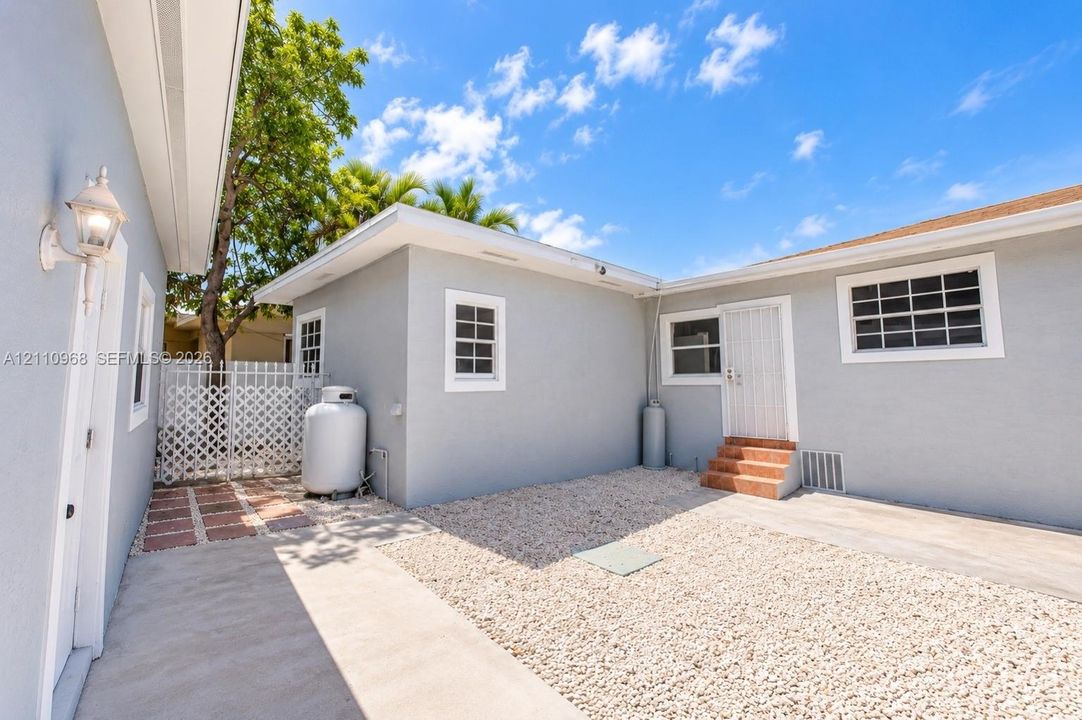 Exterior courtyard featuring light-colored stucco siding, gravel ground cover, concrete walkways, tile-accented steps, and a white lattice privacy screen