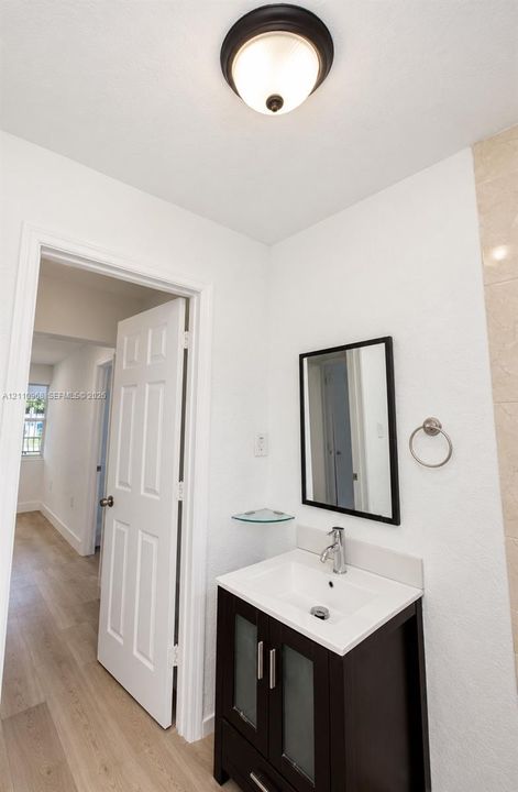 Vanity featuring a dark finish cabinet with frosted glass panel inserts, a white integrated rectangular sink, a chrome faucet, and an attached corner glass shelf