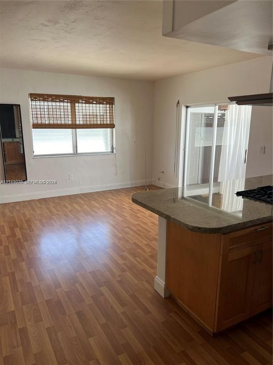 Wood-finish flooring, stone-surfaced peninsula, natural wood cabinetry, and a large multi-pane window