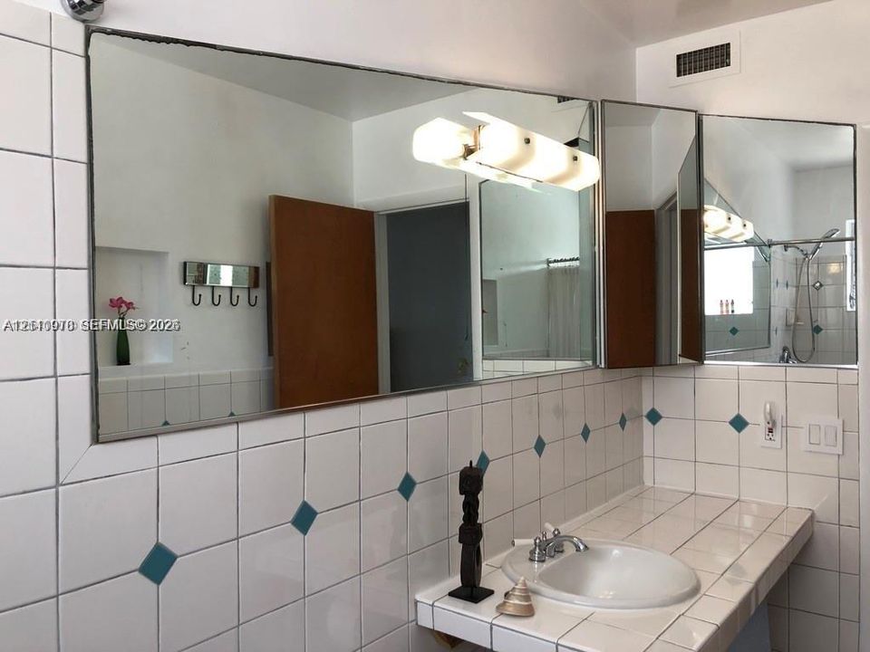 Bathroom vanity with integrated tile countertop, inset basin, polished metal hardware, expansive wall-mounted mirror, and decorative tile accents