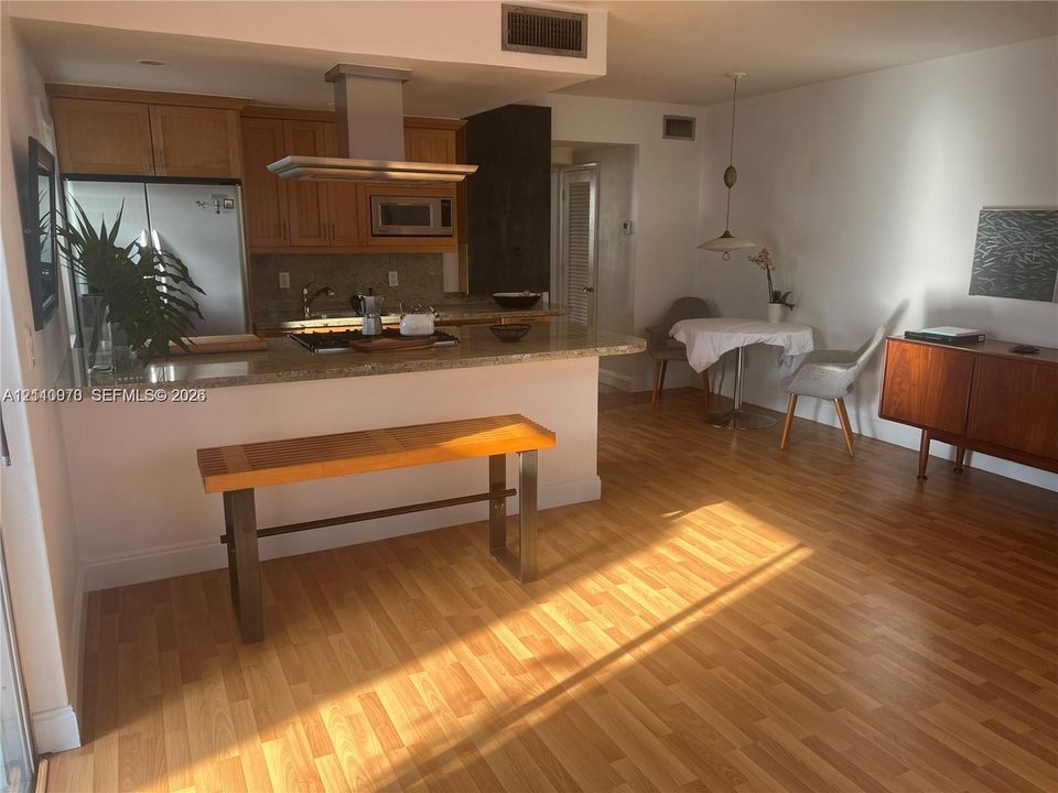 Kitchen featuring wood cabinetry, stone-surface breakfast bar, stainless steel vent hood, and wood-finish flooring