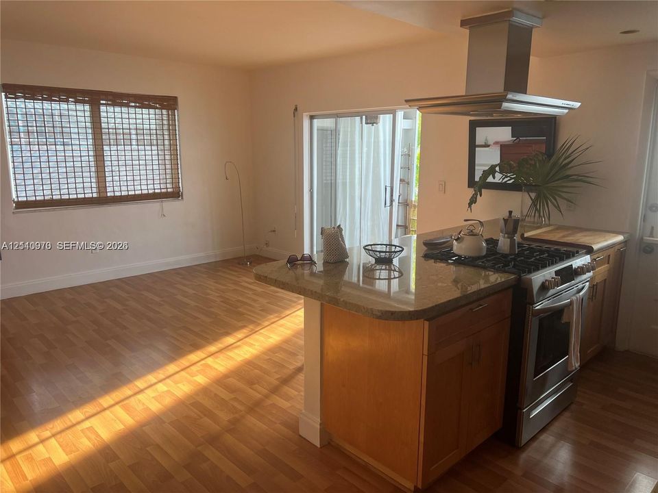 Kitchen featuring an island with a stone countertop, stainless steel gas range, stainless steel range hood, wood-finish cabinetry, and wood-finish flooring