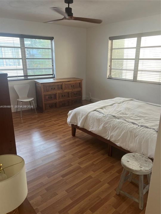 Room featuring wood-finish flooring, dual windows with horizontal blinds, and a ceiling fan