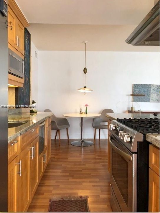 Kitchen featuring wood-finish cabinetry, natural stone countertops, stainless steel gas range, overhead range hood, and wood-finish flooring