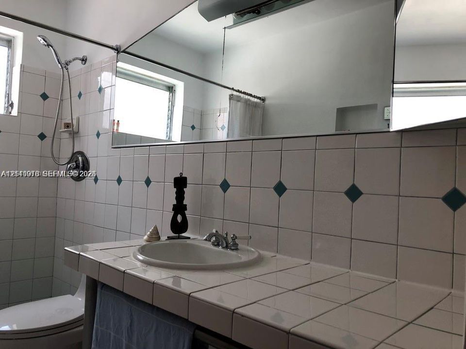 Tiled vanity with an integrated basin, chrome-finish dual-handle faucet, full-width wall mirror, and tiled walls featuring decorative insets