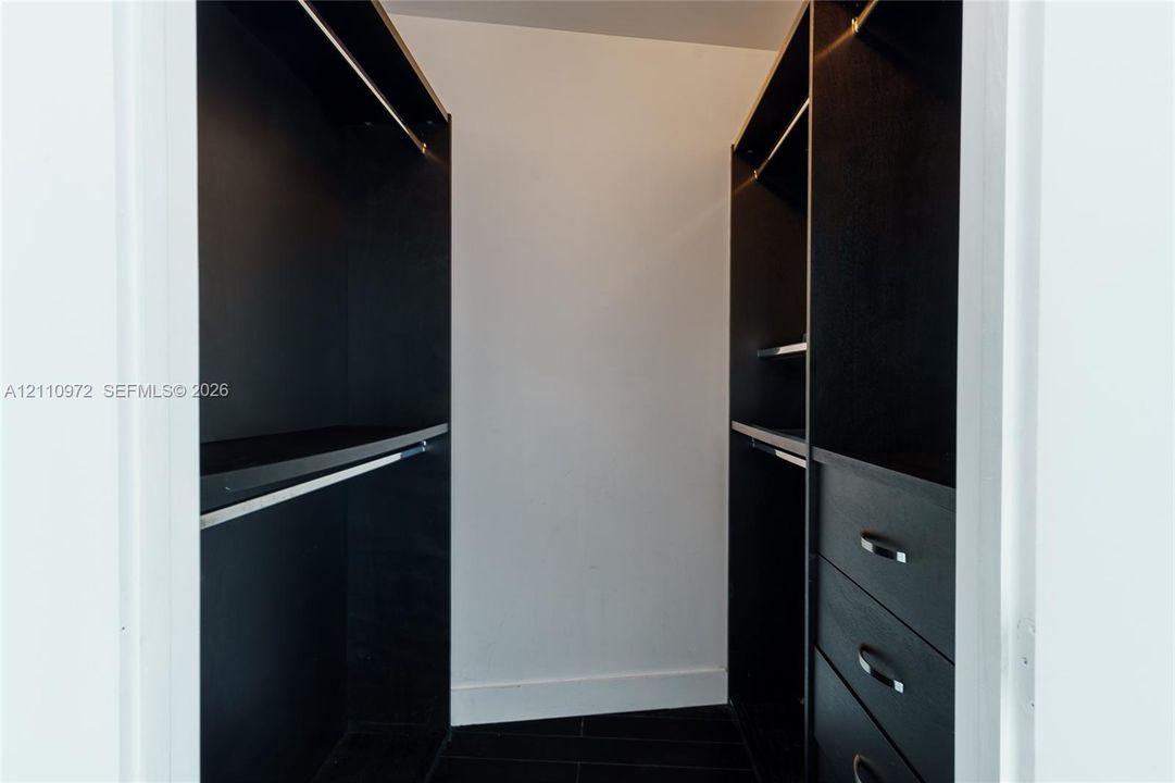 Built-in closet featuring matte black cabinetry, integrated shelving, hanging rods, and a three-drawer chest unit