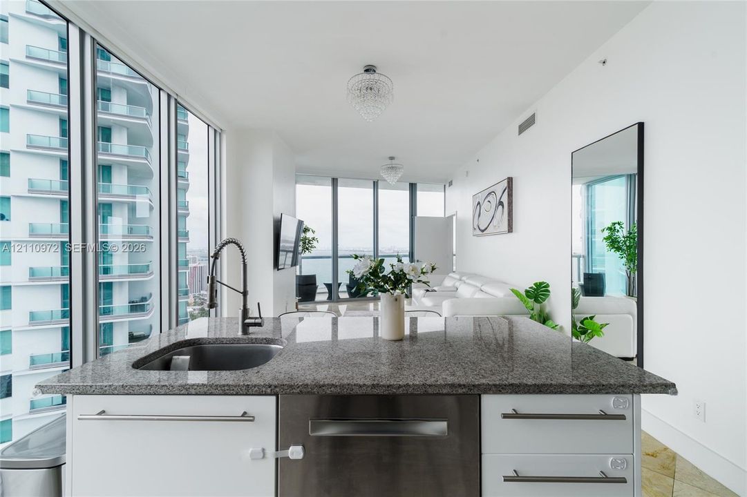 Kitchen island featuring stone countertops, an undermount sink, stainless steel dishwasher, and white cabinetry with metal hardware