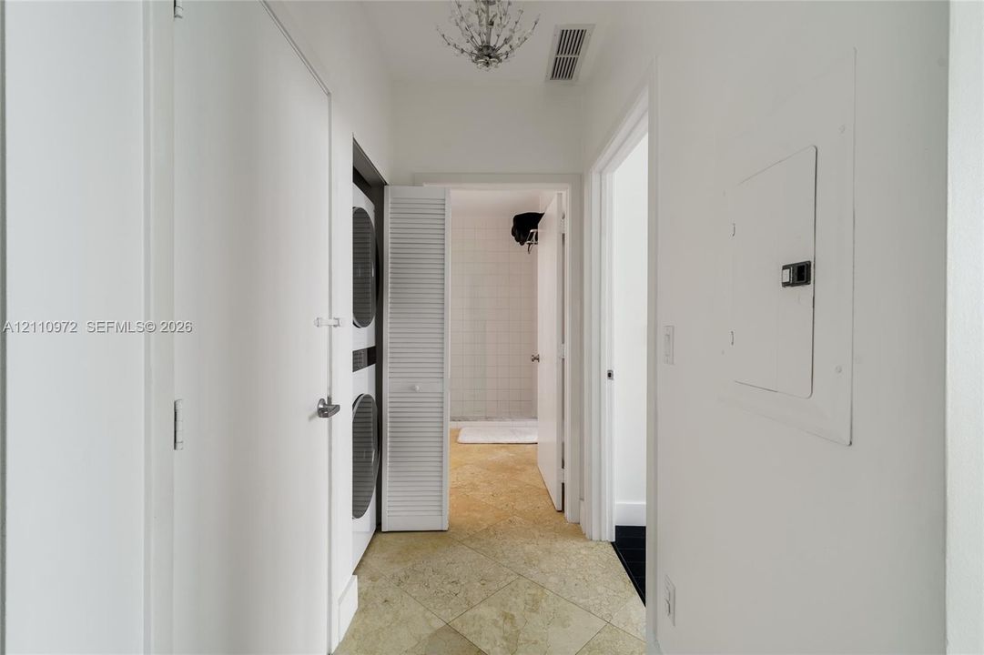 Hallway featuring stone-finish tile flooring, a decorative ceiling-mounted chandelier, and an integrated laundry closet with louvered doors