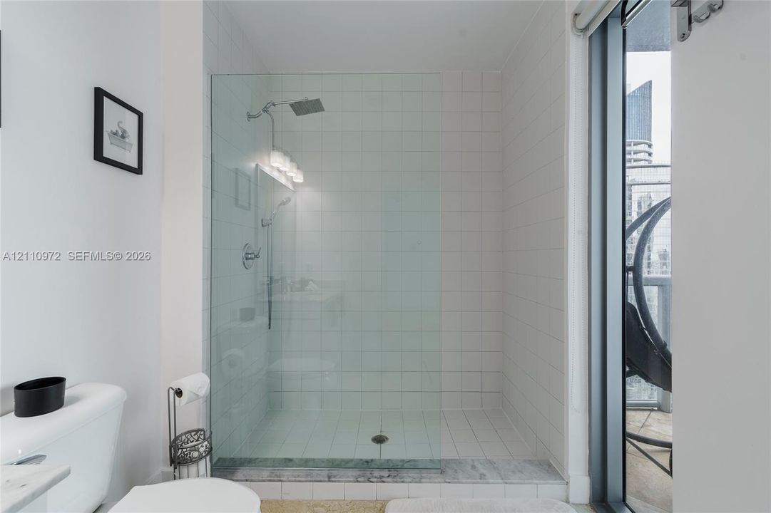 Walk-in shower featuring a glass enclosure, wall-mounted rainfall showerhead, handheld shower wand, and white square-tile surround with a stone threshold