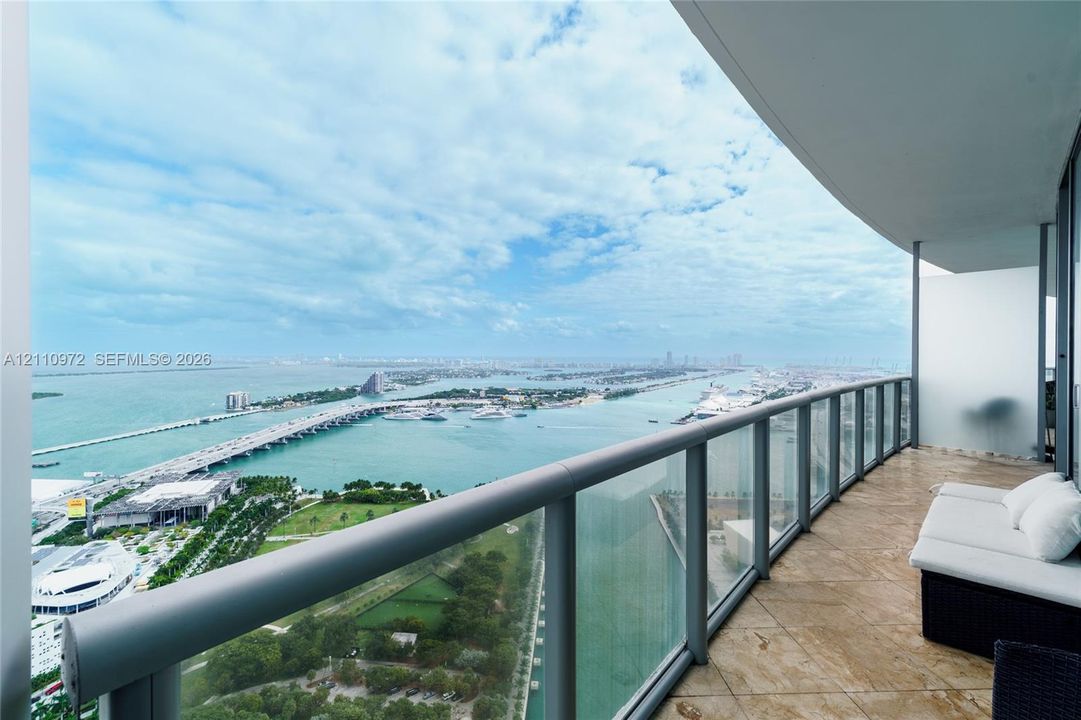 Spacious covered balcony with stone-finish flooring and a glass-paneled railing