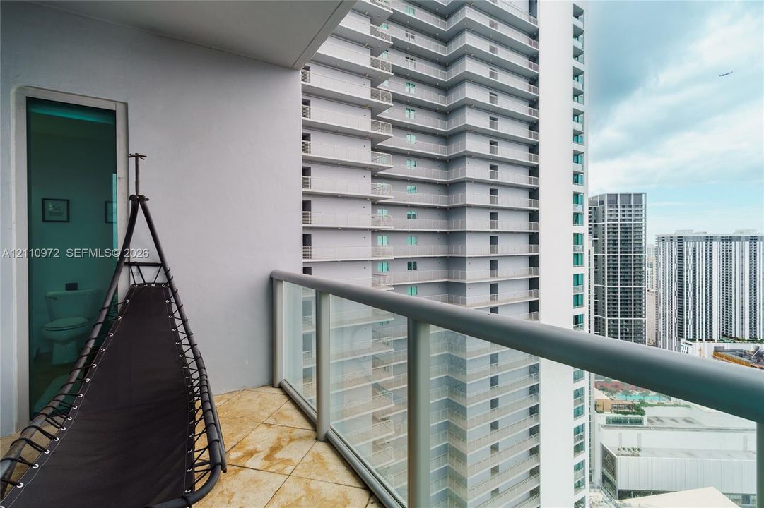 Covered balcony featuring tile flooring and a glass-panel railing with metal frame