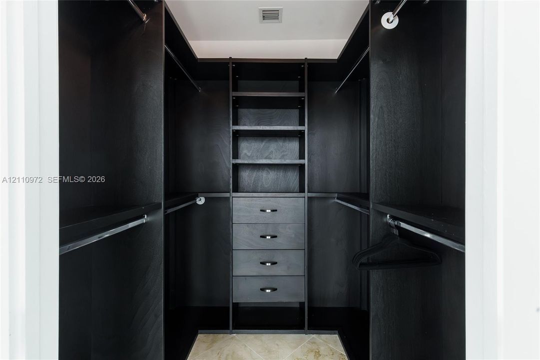 Custom walk-in closet featuring dark wood-finish cabinetry, built-in shelving, four integrated storage drawers, and polished metal hardware