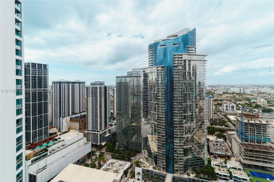 High-rise urban cityscape featuring blue glass curtain wall architecture, multiple steel-and-glass towers, and structured building balconies