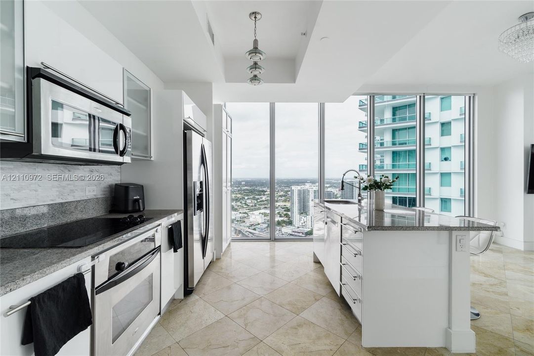 Kitchen featuring white cabinetry, stone countertops, stainless steel appliances, a center island, and floor-to-ceiling windows