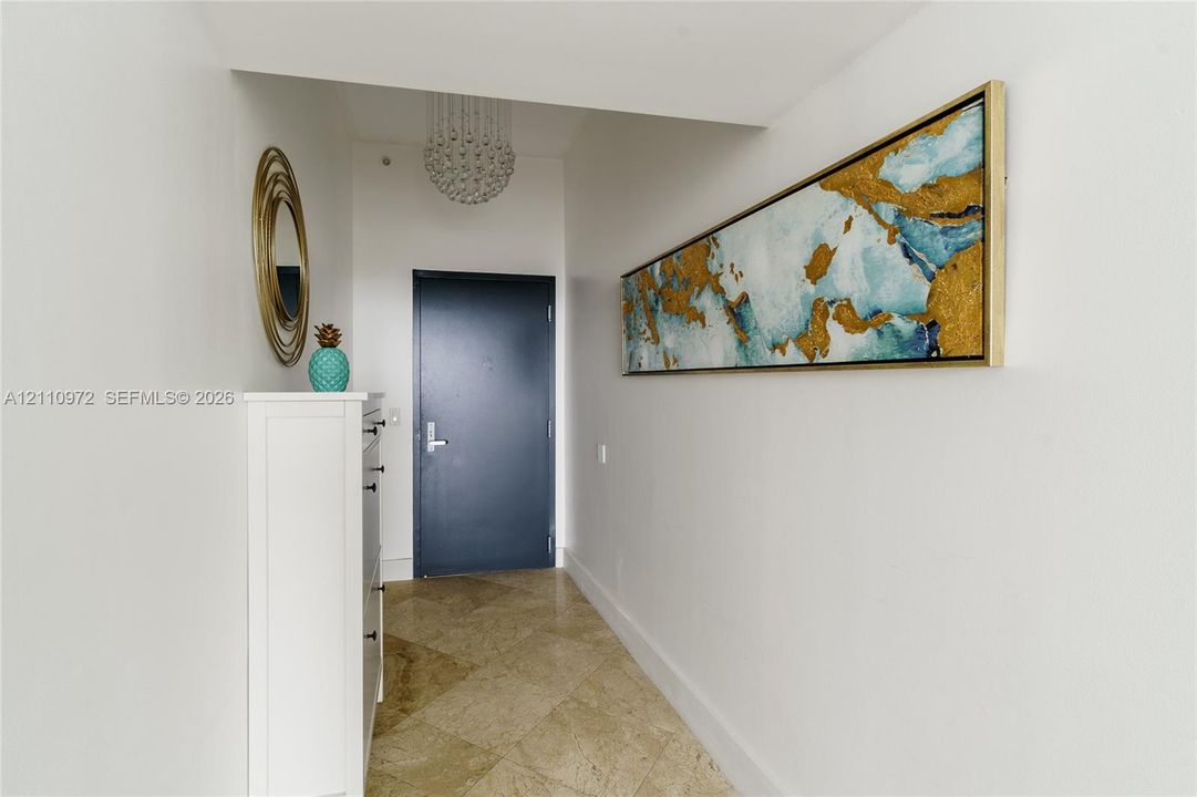 Entryway featuring diagonal-set stone tile flooring, a tiered crystal drum chandelier, and a solid-core door with brushed metal hardware