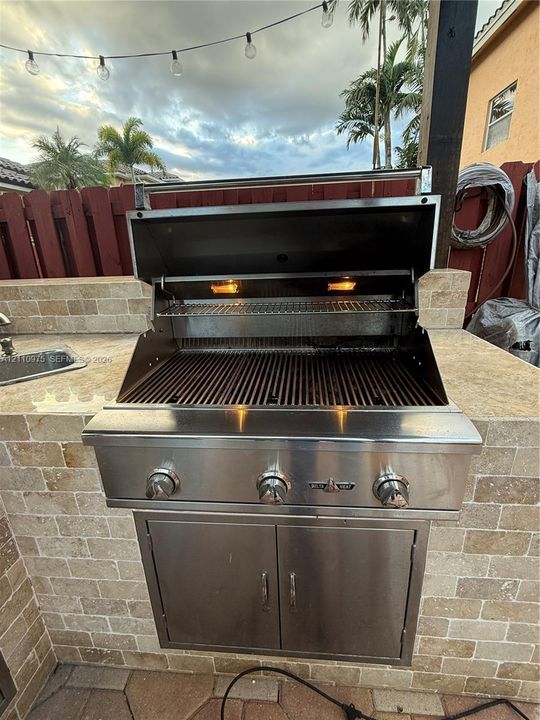 Outdoor kitchen featuring a built-in stainless steel grill, natural stone masonry surround, integrated stainless steel storage cabinet, and an inset sink