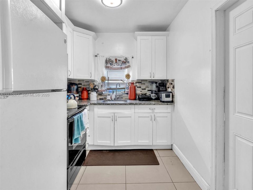 Kitchen featuring white cabinetry, stone-surface countertops, mosaic tile backsplash, stainless steel sink, and ceramic tile flooring