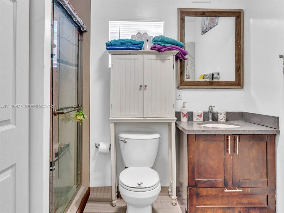 Bathroom vanity with dark wood-finish cabinetry, solid surface countertop, integrated sink, and glass-enclosed shower