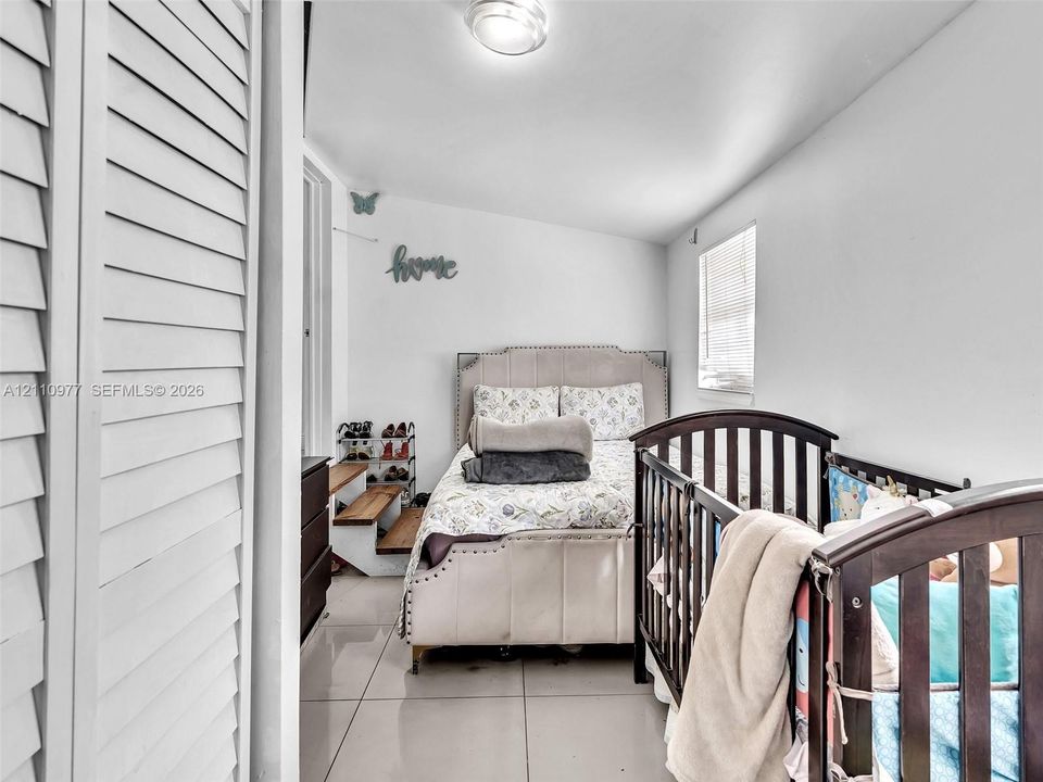 Large-format tile flooring, white louvered closet doors, and a window with horizontal blinds