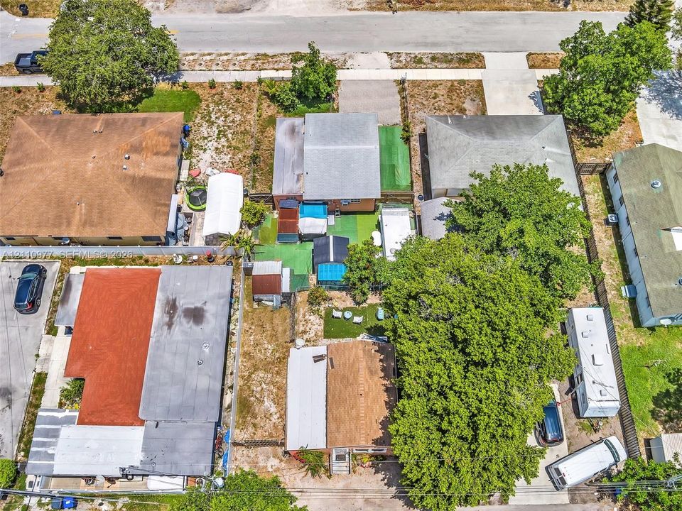 Aerial view of the residential property featuring a composition shingle roof, mature tree coverage, and an expansive exterior lot