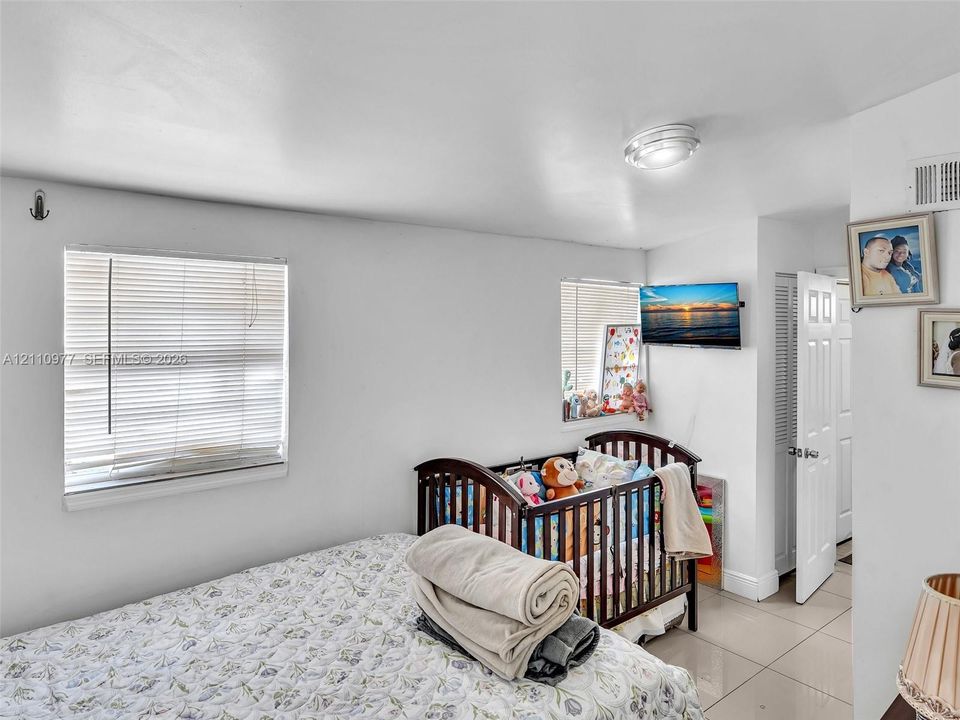 Neutral-toned room featuring large-format tile flooring, recessed ceiling lighting, two horizontal windows with fitted blinds, and a paneled interior door