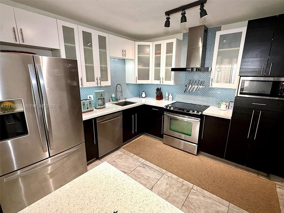 Kitchen featuring dual-tone cabinetry, stainless steel appliances, blue glass tile backsplash, stone-surface countertops, and track lighting