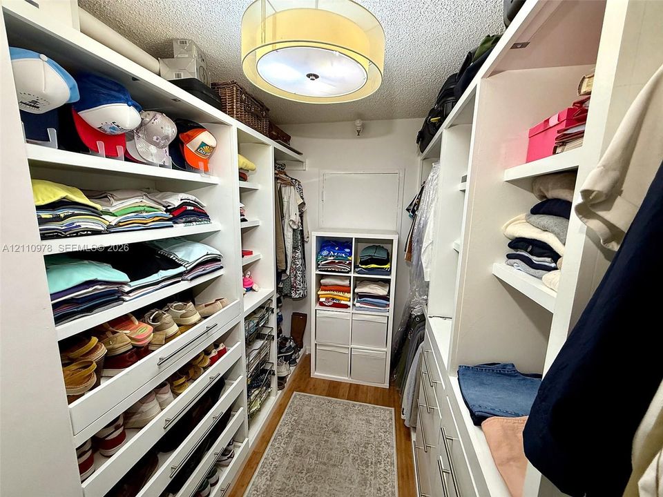Custom walk-in closet featuring extensive white built-in shelving, integrated storage drawers with polished hardware, wood flooring, and a drum-style ceiling light fixture
