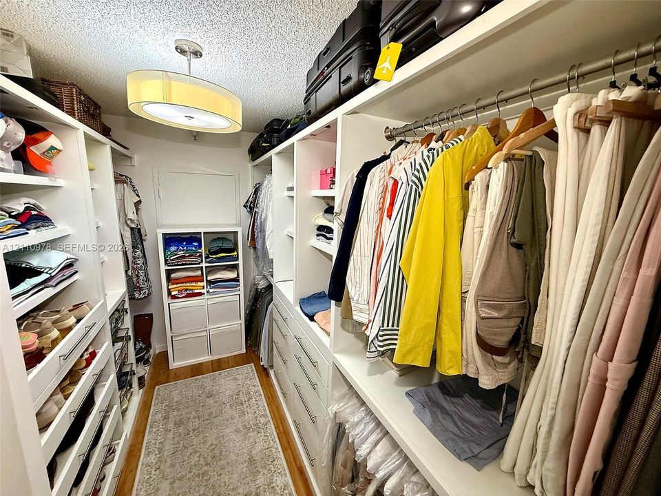 Walk-in closet featuring white built-in cabinetry, multiple adjustable shelving tiers, integrated hanging rods, and an overhead drum lighting fixture