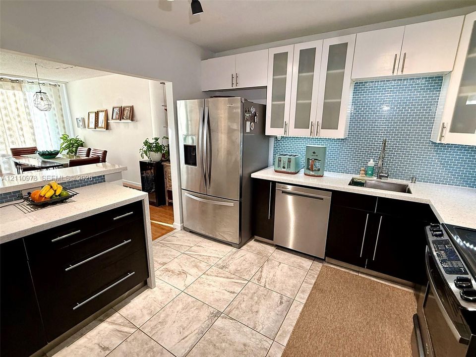 Kitchen featuring high-contrast dark lower cabinetry with white upper cabinets, quartz countertops, a blue glass tile backsplash, and stainless steel appliances