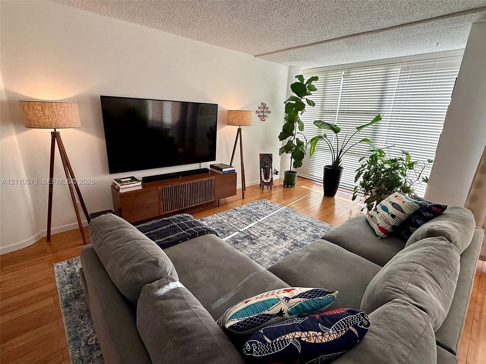 Living area featuring wood-finish flooring and expansive floor-to-ceiling windows with horizontal blinds