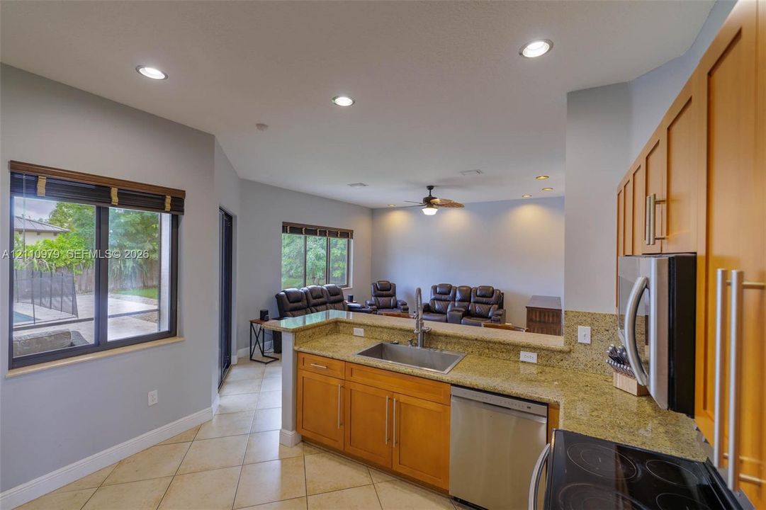 Kitchen featuring honey-toned wood cabinetry, stone countertops, stainless steel appliances, tile flooring, and recessed lighting