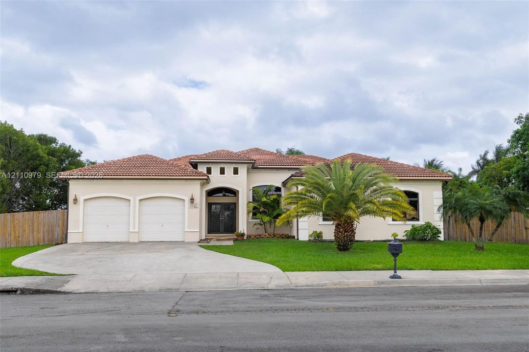 Single-story stucco residence featuring a multi-gabled clay tile roof, two-car garage, arched entryway, and concrete driveway