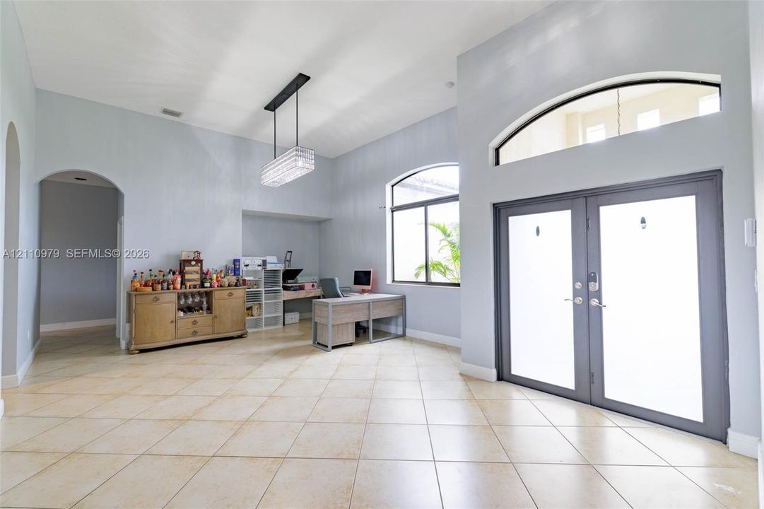 High-ceiling foyer featuring tile flooring, double-door entrance with an arched transom window, and a modern rectangular pendant light fixture